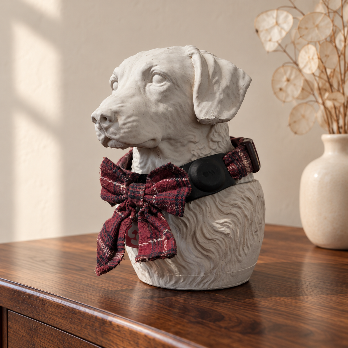 Three-quarter view of a white cast stone dog urn with a tartan collar and bow.