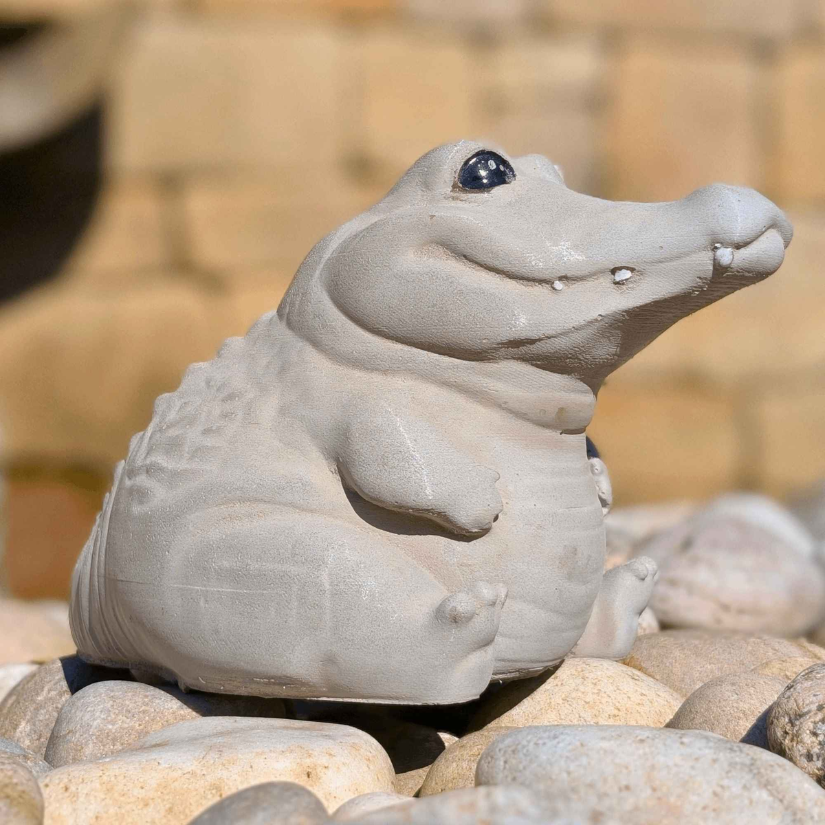 Cast stone crocodile garden ornament sitting among pale pebbles