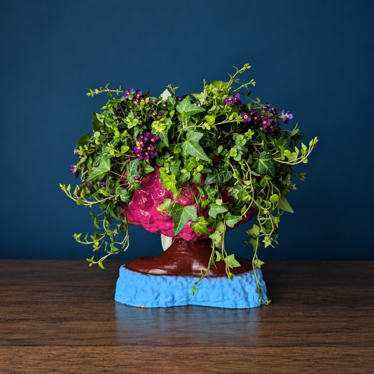 Girl Juice head planter filled with trailing greenery against a deep blue wall