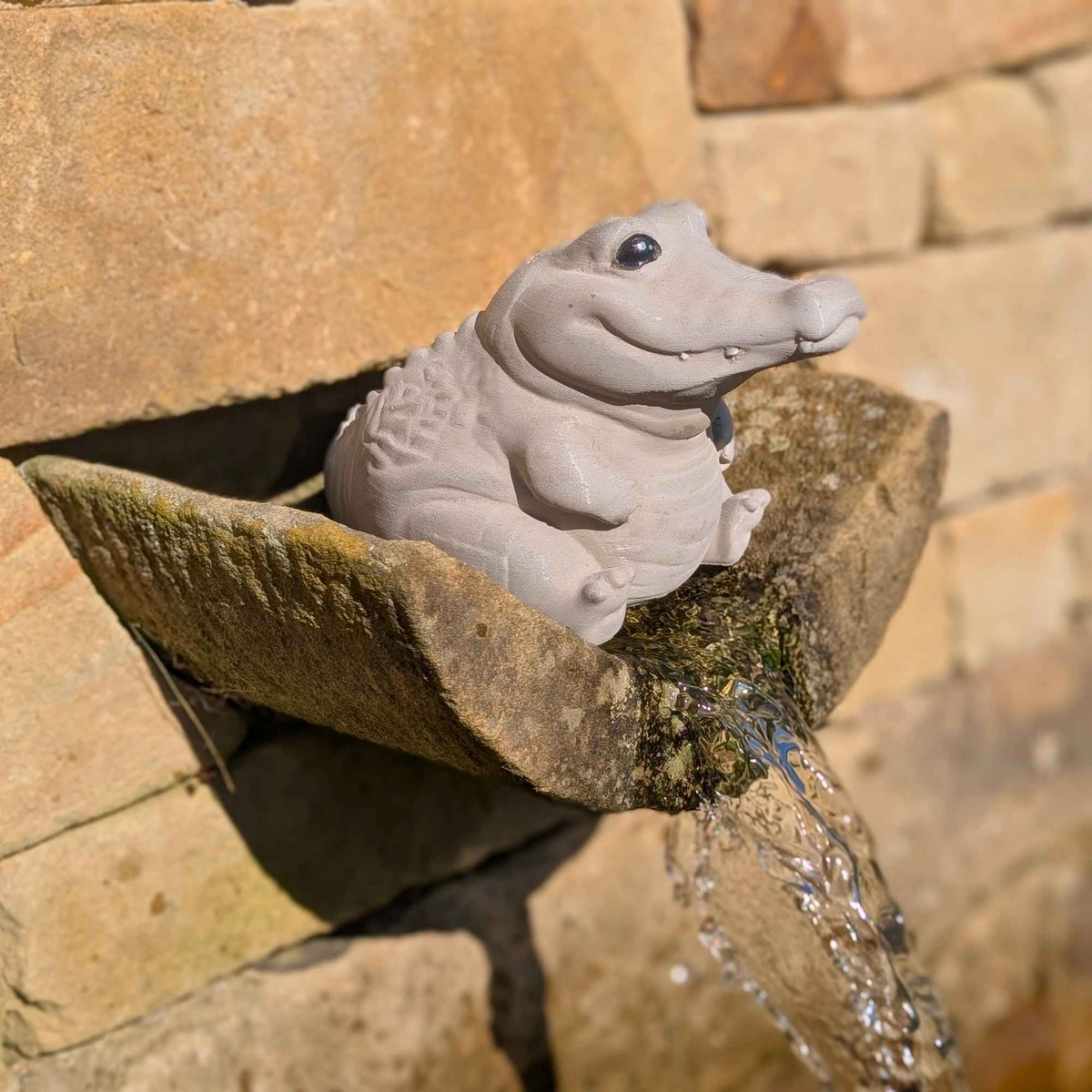 Cast stone crocodile ornament perched by a flowing stone water spout