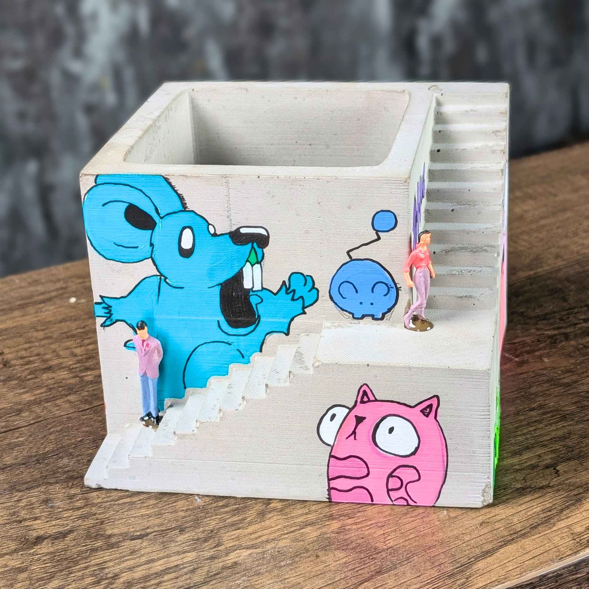 Empty graffiti building planter showing blue mural, pink character and staircase