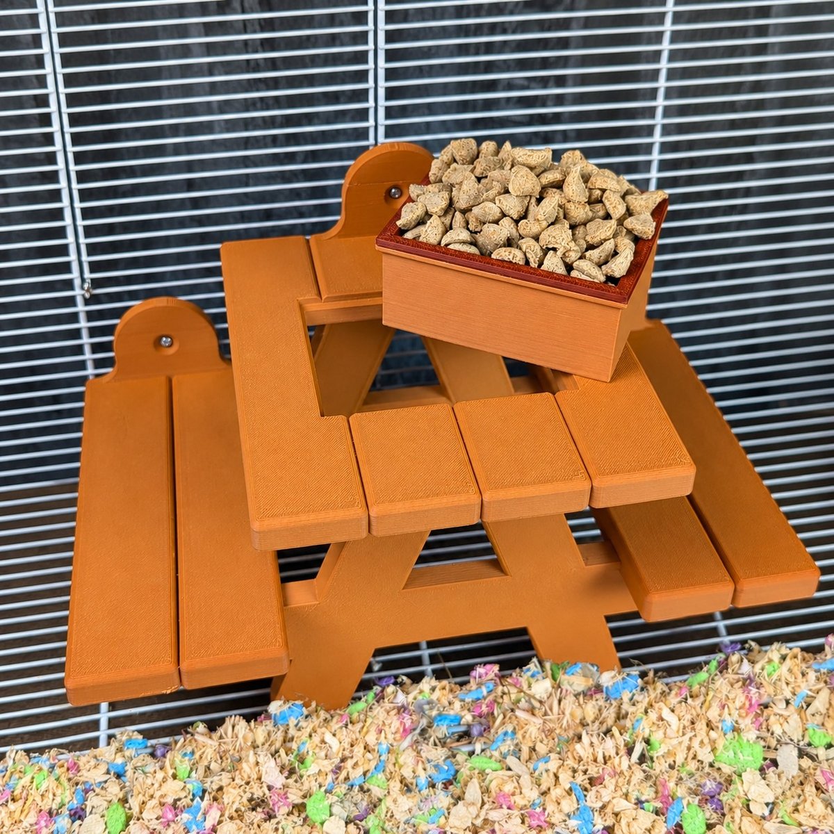 Orange rat picnic bench with filled food bowl attached inside a cage