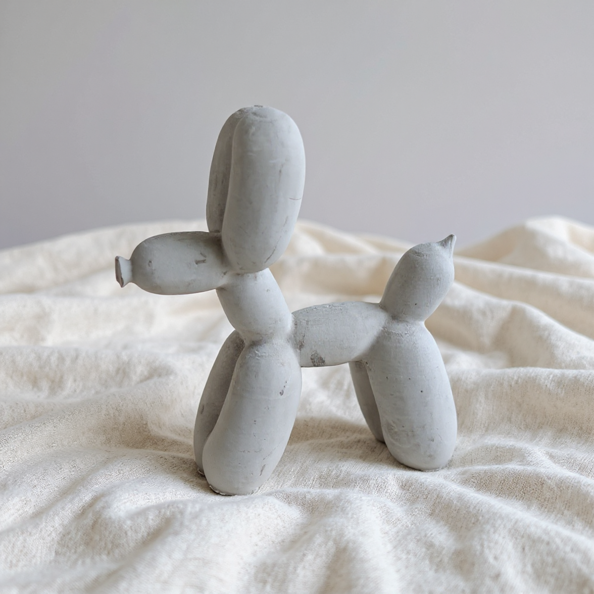 Side view of cast stone balloon dog ornament on soft white fabric