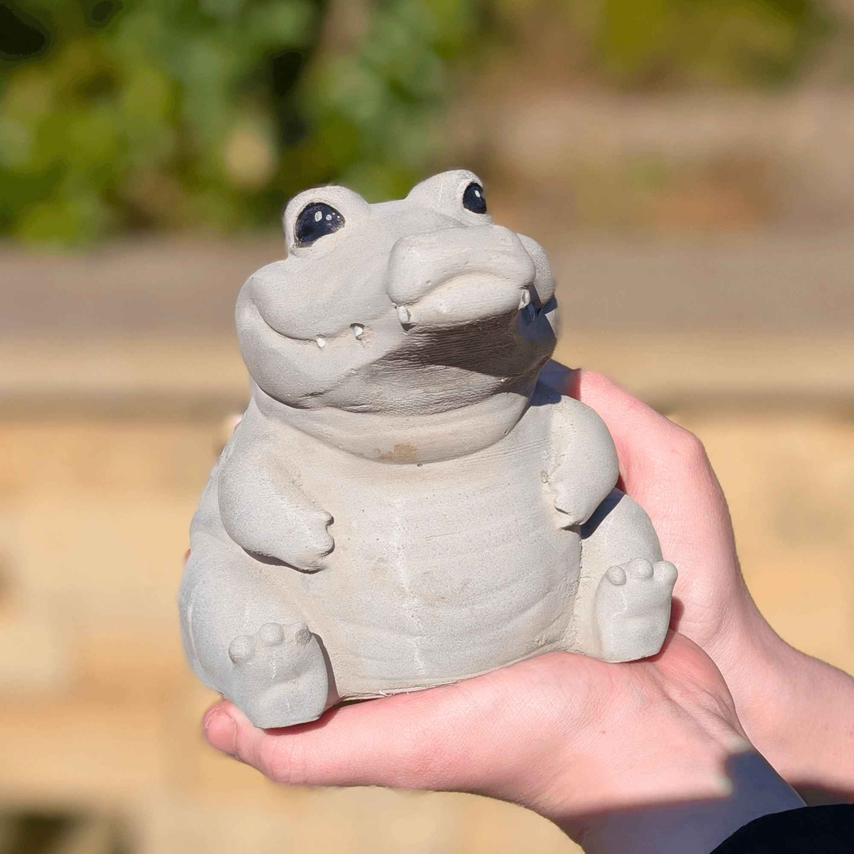 Front view of the smiling cast stone crocodile ornament held outdoors