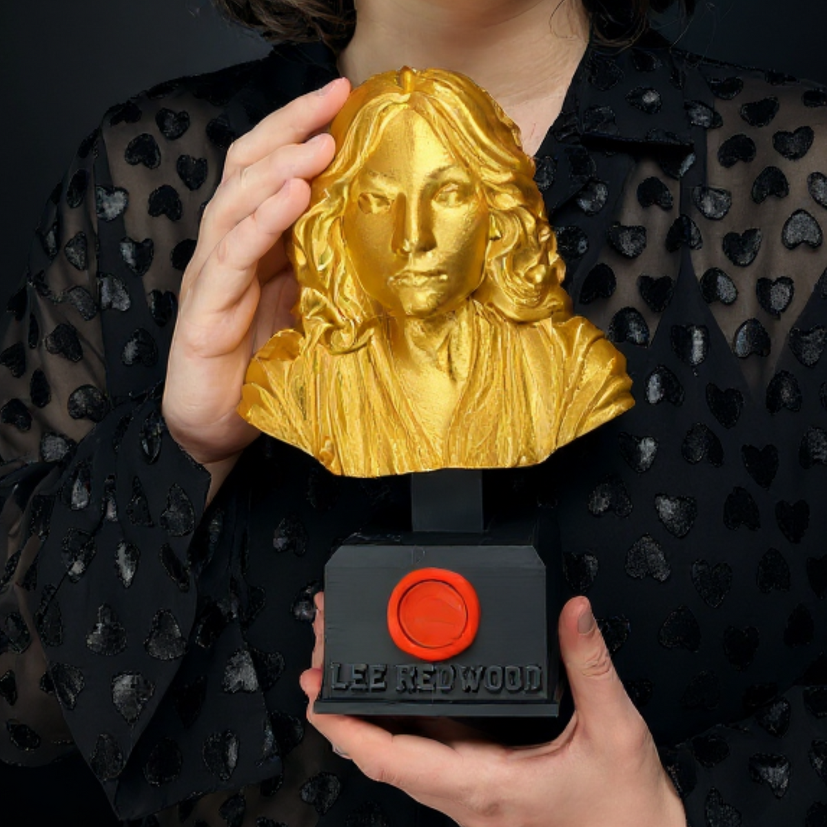 Person holding a personalised gold portrait bust trophy with black engraved base