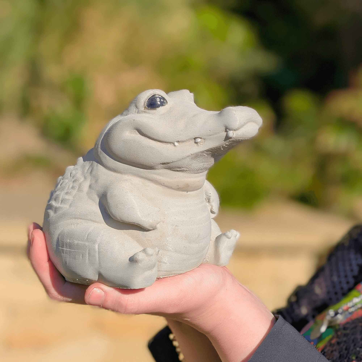 Cast stone crocodile garden ornament held in one hand for scale