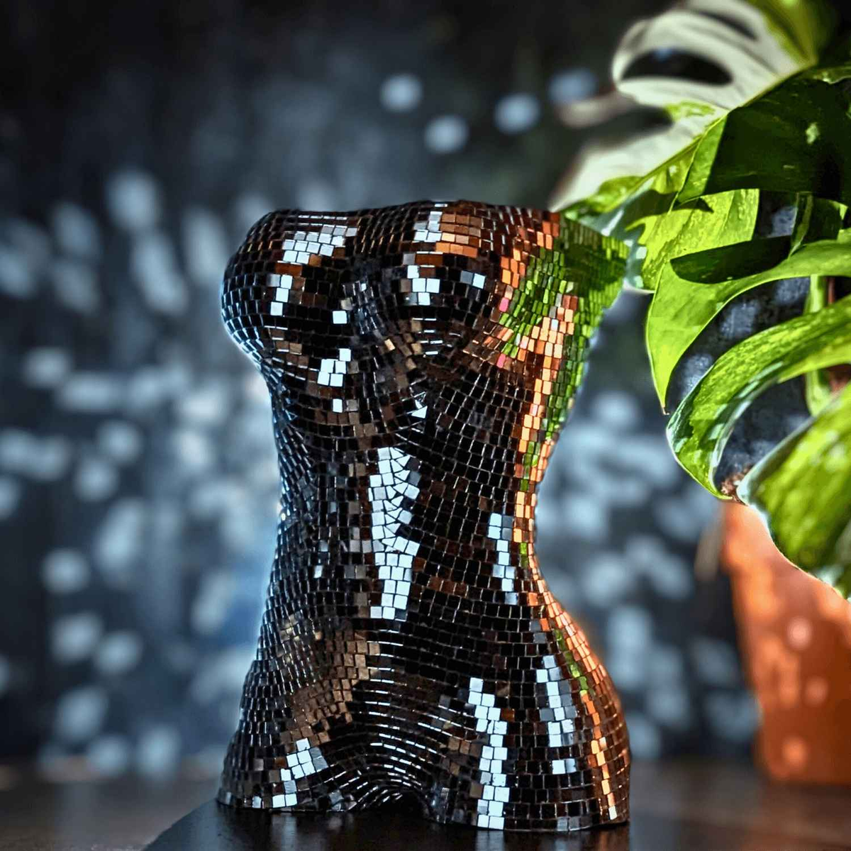 Silver mirror mosaic torso planter beside a monstera leaf, side view