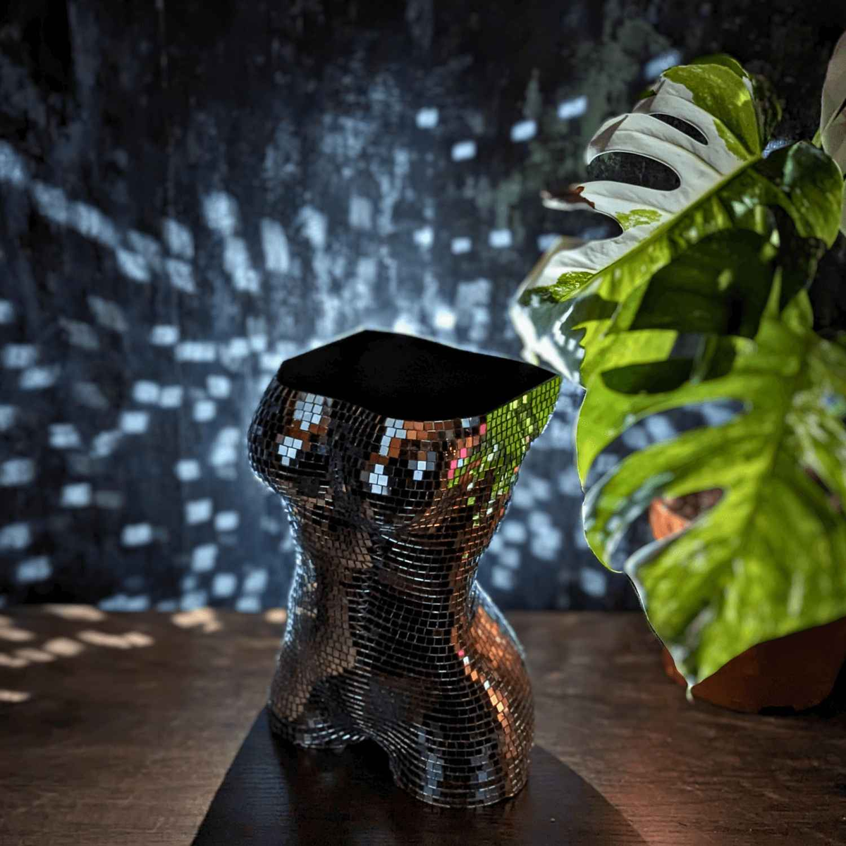 Mirror torso planter beside a monstera in dappled light