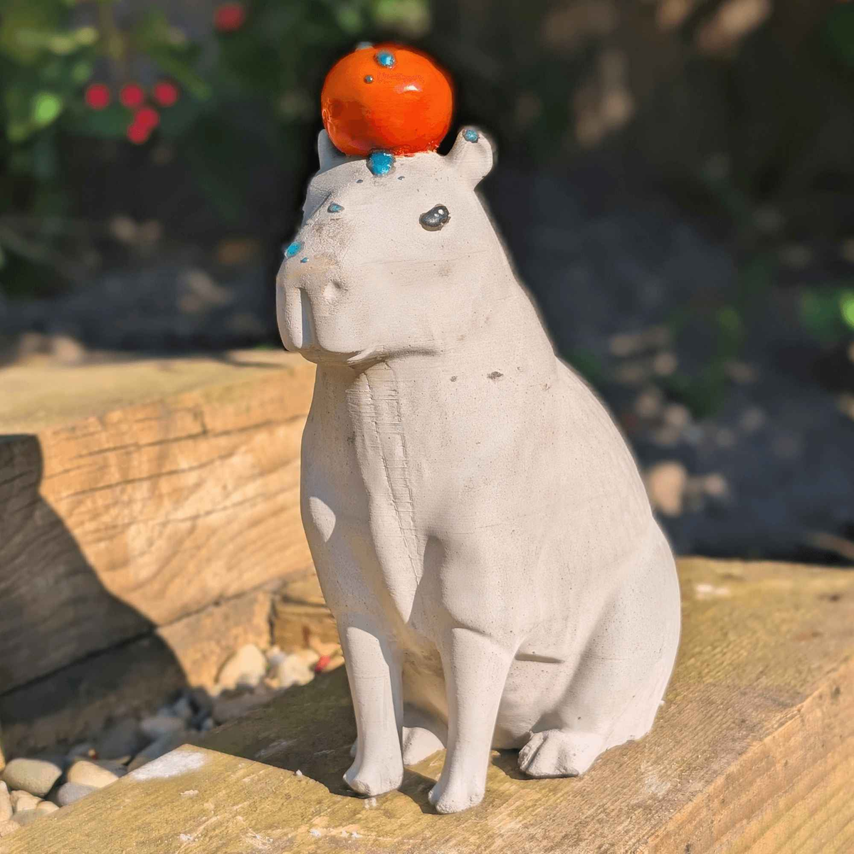 Front view of cast stone capybara with orange in a sunny garden