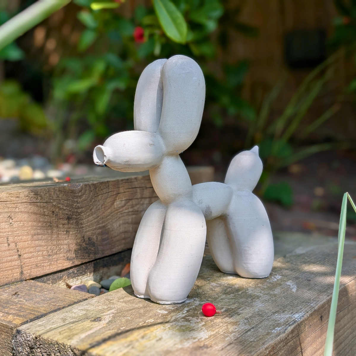 Balloon dog garden ornament on a wooden bench beside a red ball