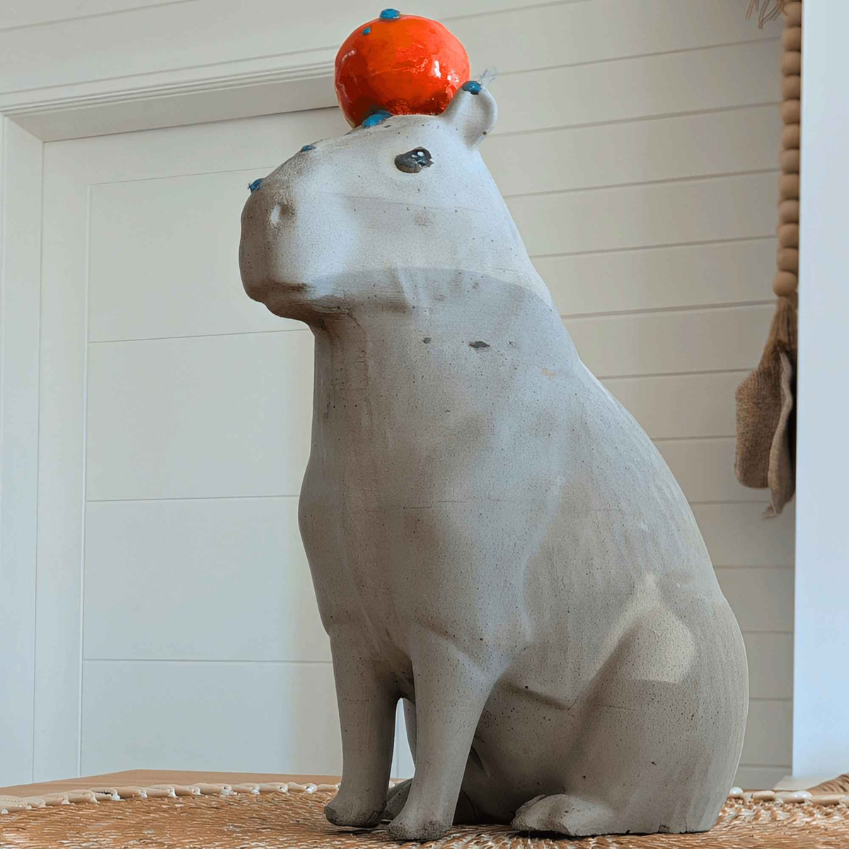 Cast stone capybara with orange, side profile on an indoor shelf