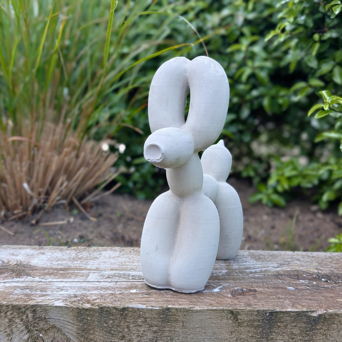 Cast stone balloon dog ornament on a stone ledge in a garden