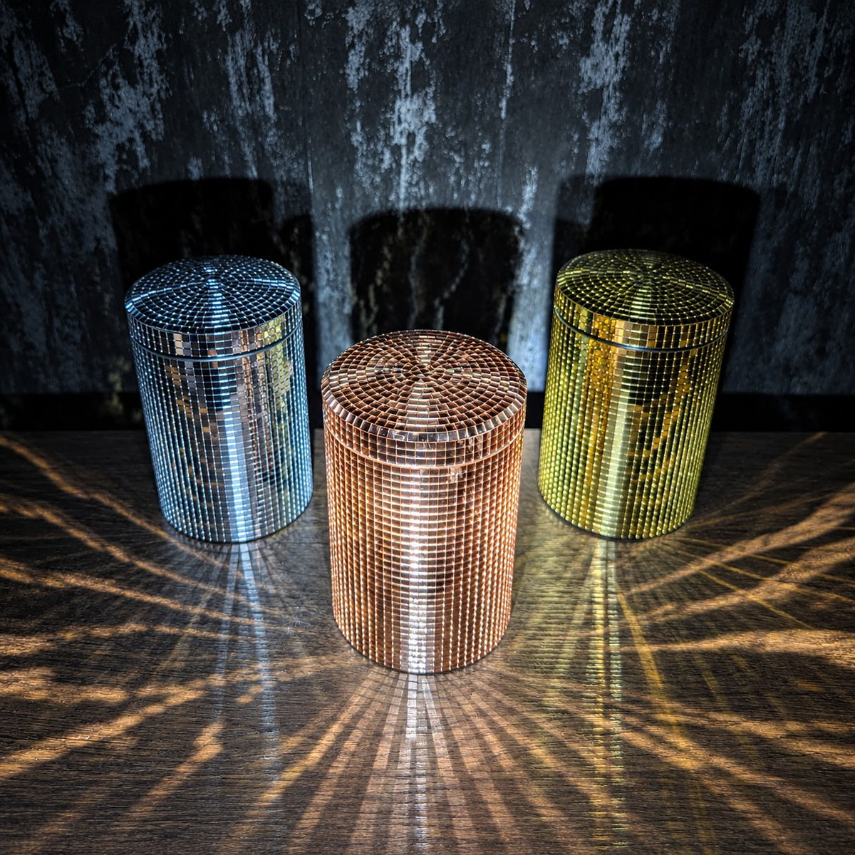 Silver, rose gold and gold mirror canisters reflecting light in a dark setting