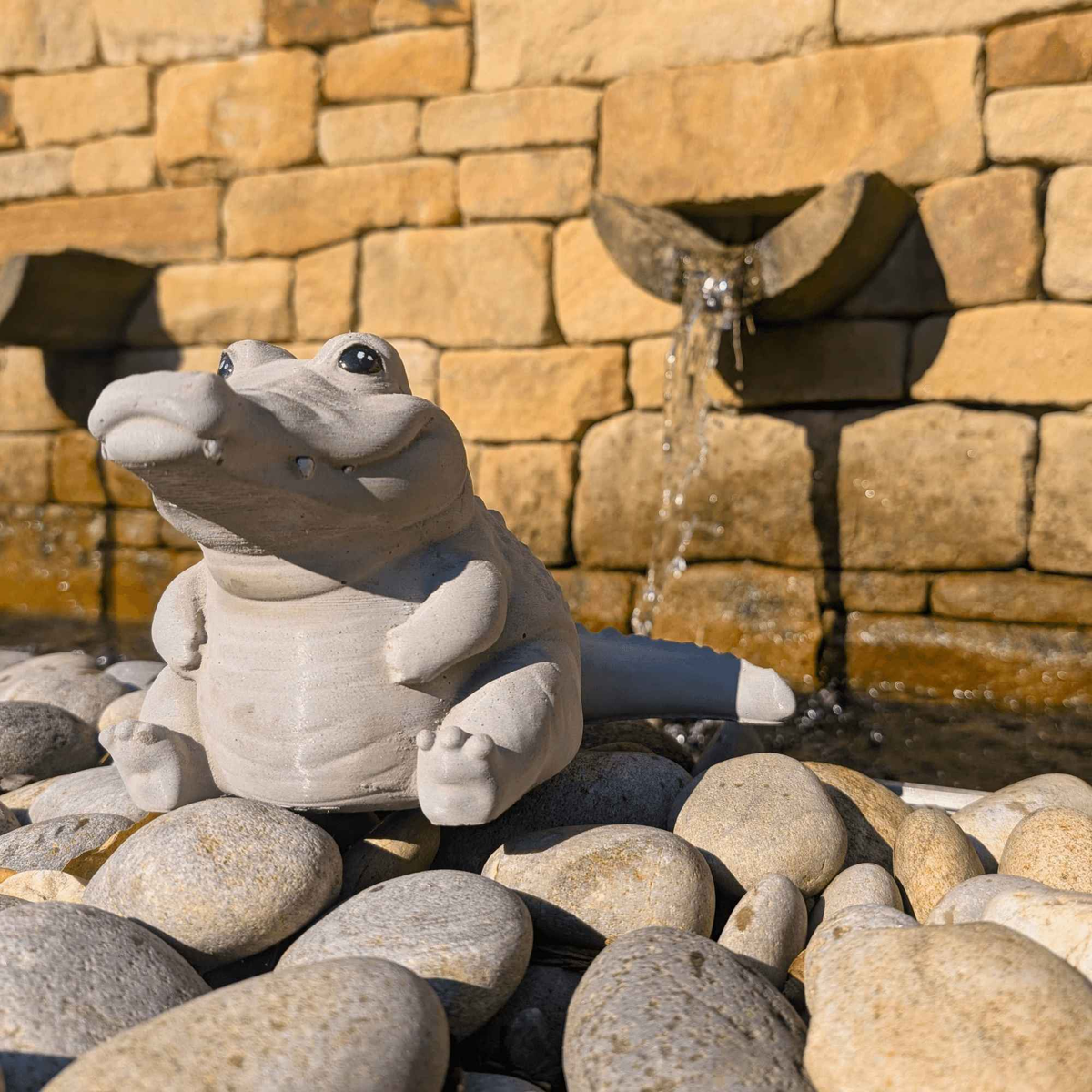 Crocodile garden ornament beside a stone water feature and pebbles