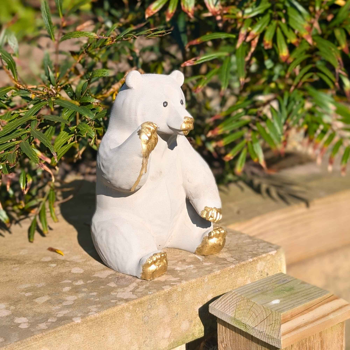 Side view of honey bear garden ornament showing raised gold paw and seated shape