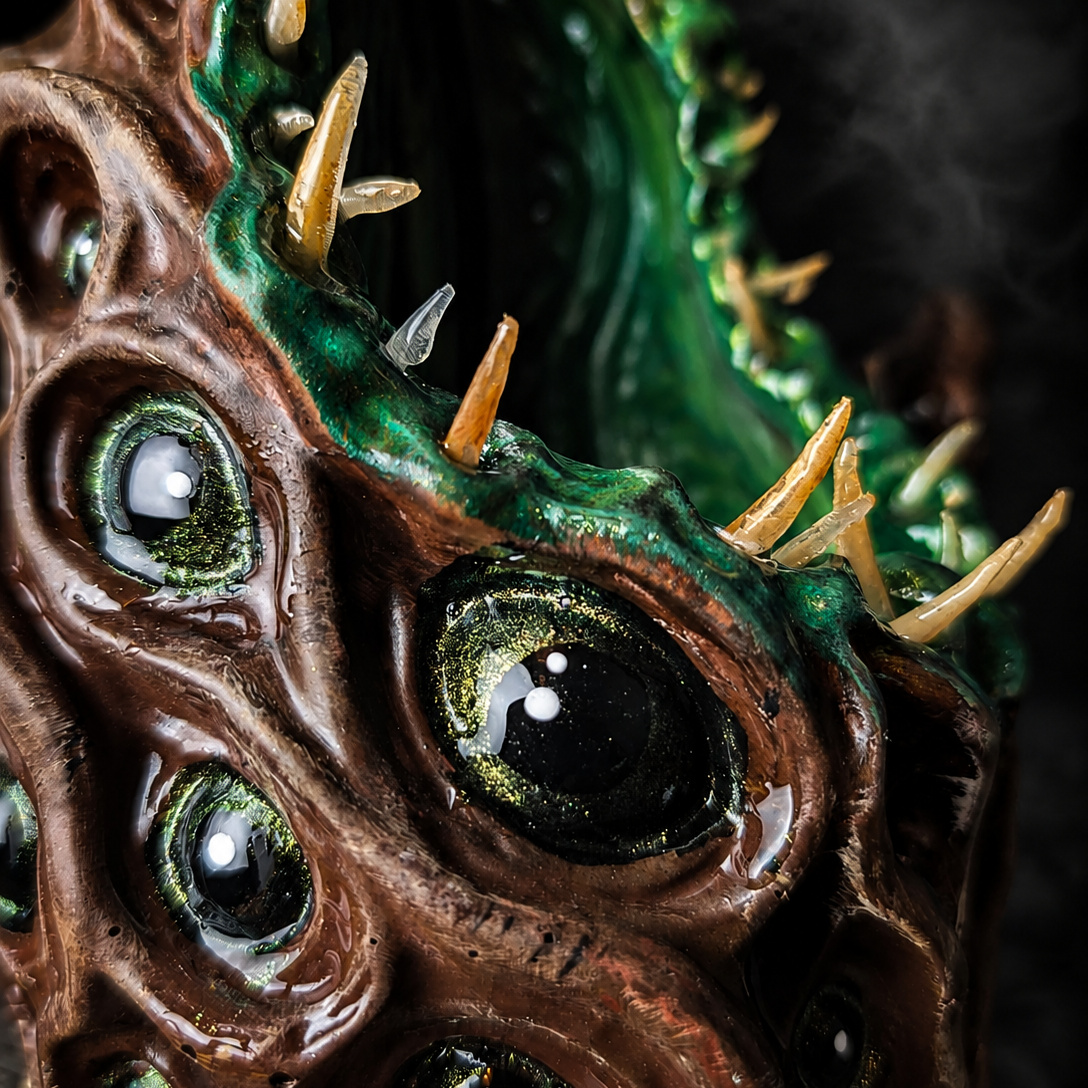 Close detail of The Watching Maw glossy black-and-gold eyes and pale teeth