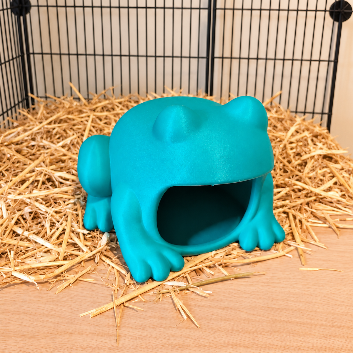 Elevated view of a turquoise frog-shaped hide on a straw-covered shelf.