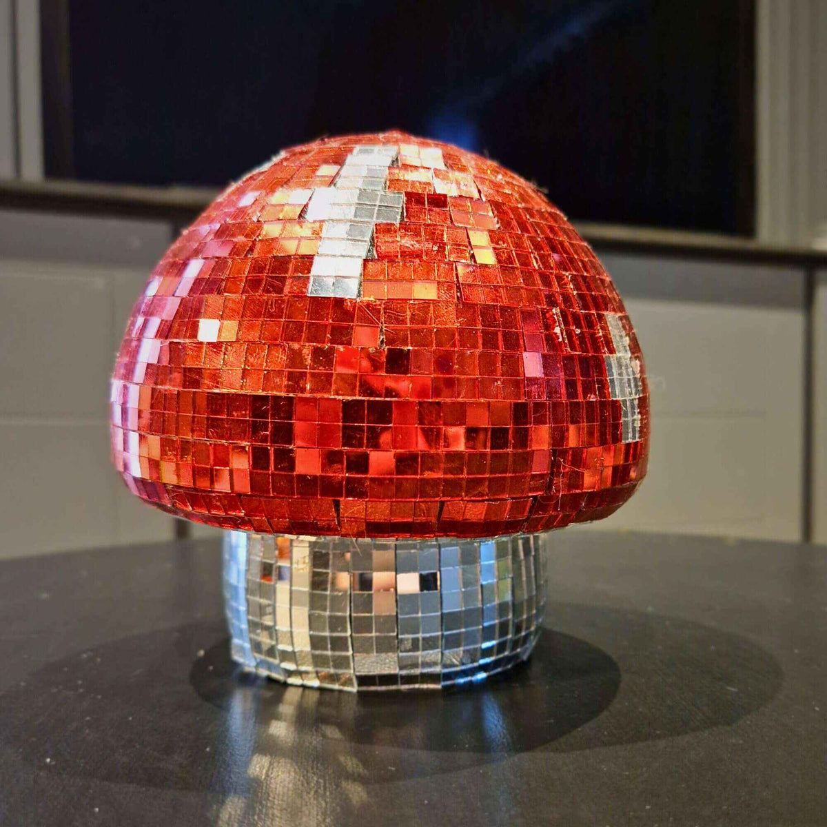 Cherry red and silver disco mushroom ornament on a dark tabletop