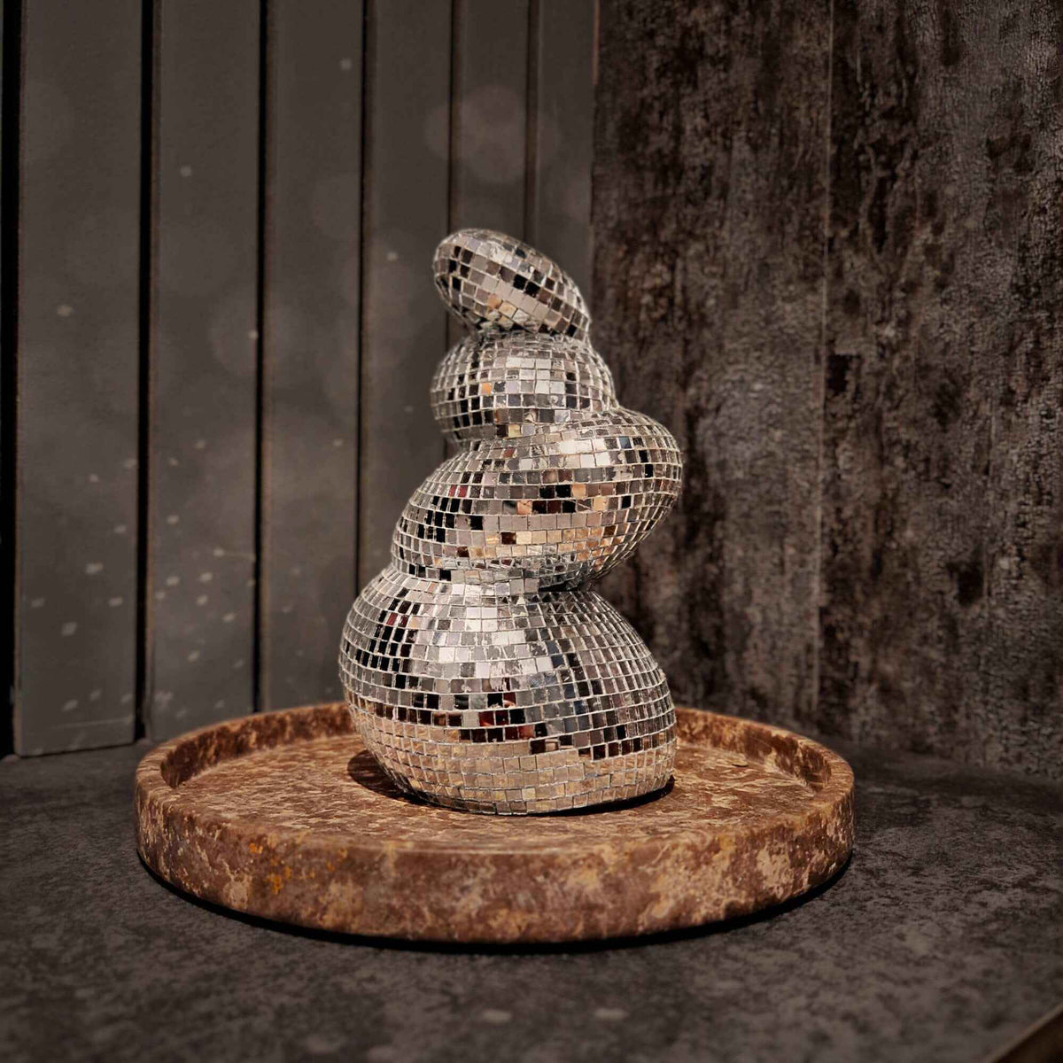 Curved mirror ball flower vase without flowers on a stone tray